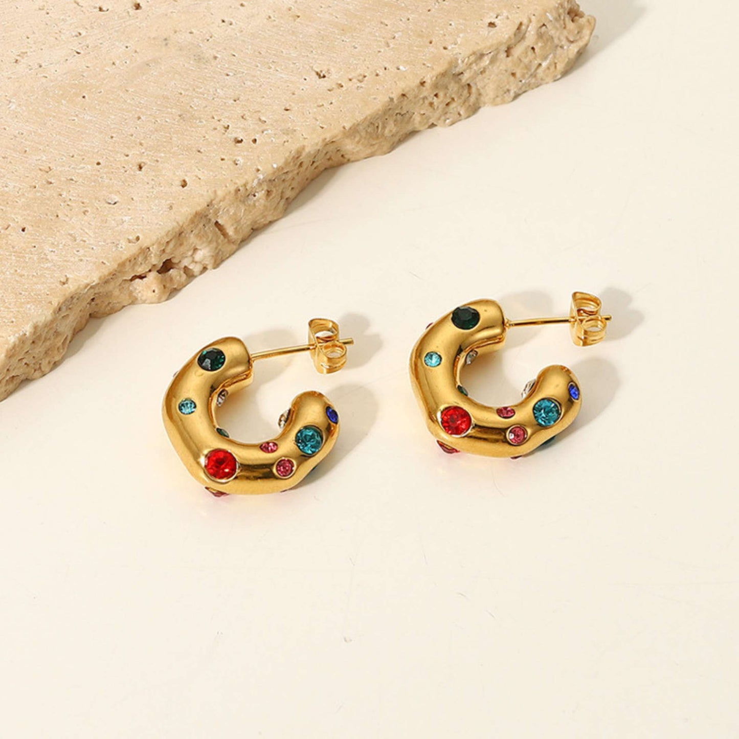 Gold hoop earrings with colorful gemstones on a light beige background