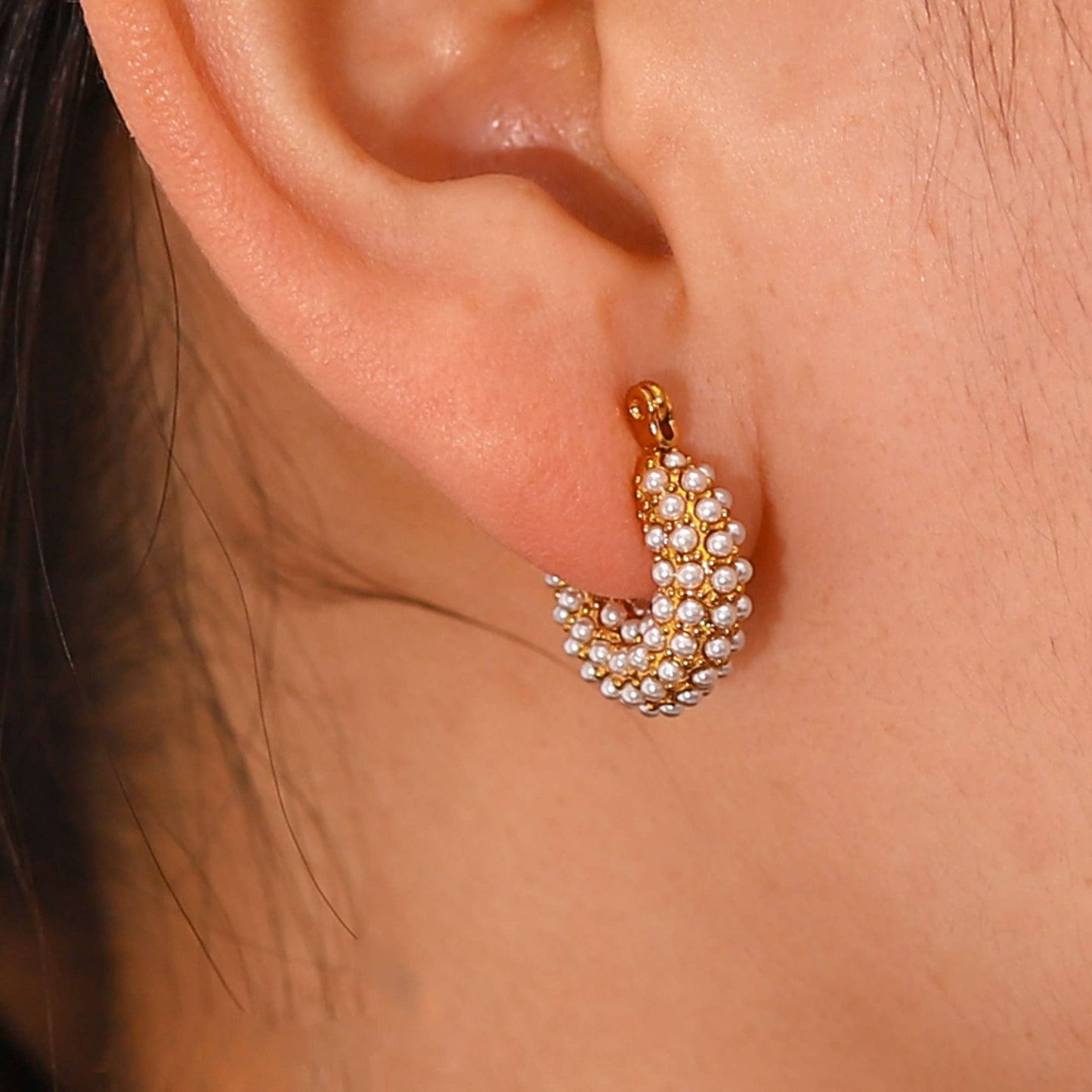 Gold and pearl hoop earring worn on an ear