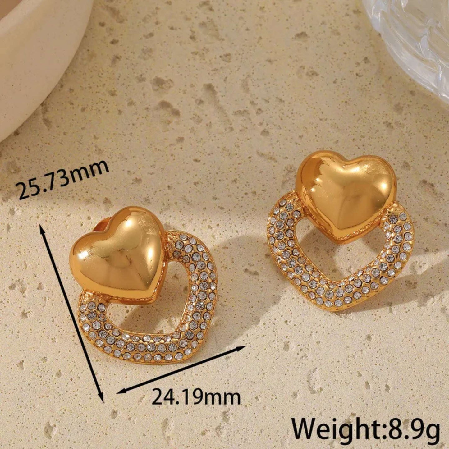 Gold heart-shaped earrings with measurements and weight on a beige surface