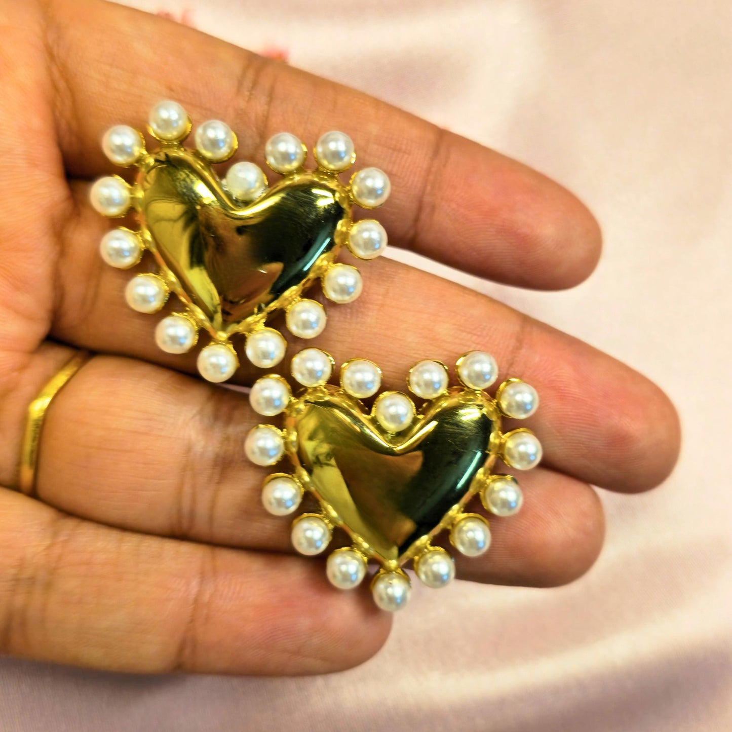 Heart-shaped object with pearls held in a hand against a light background