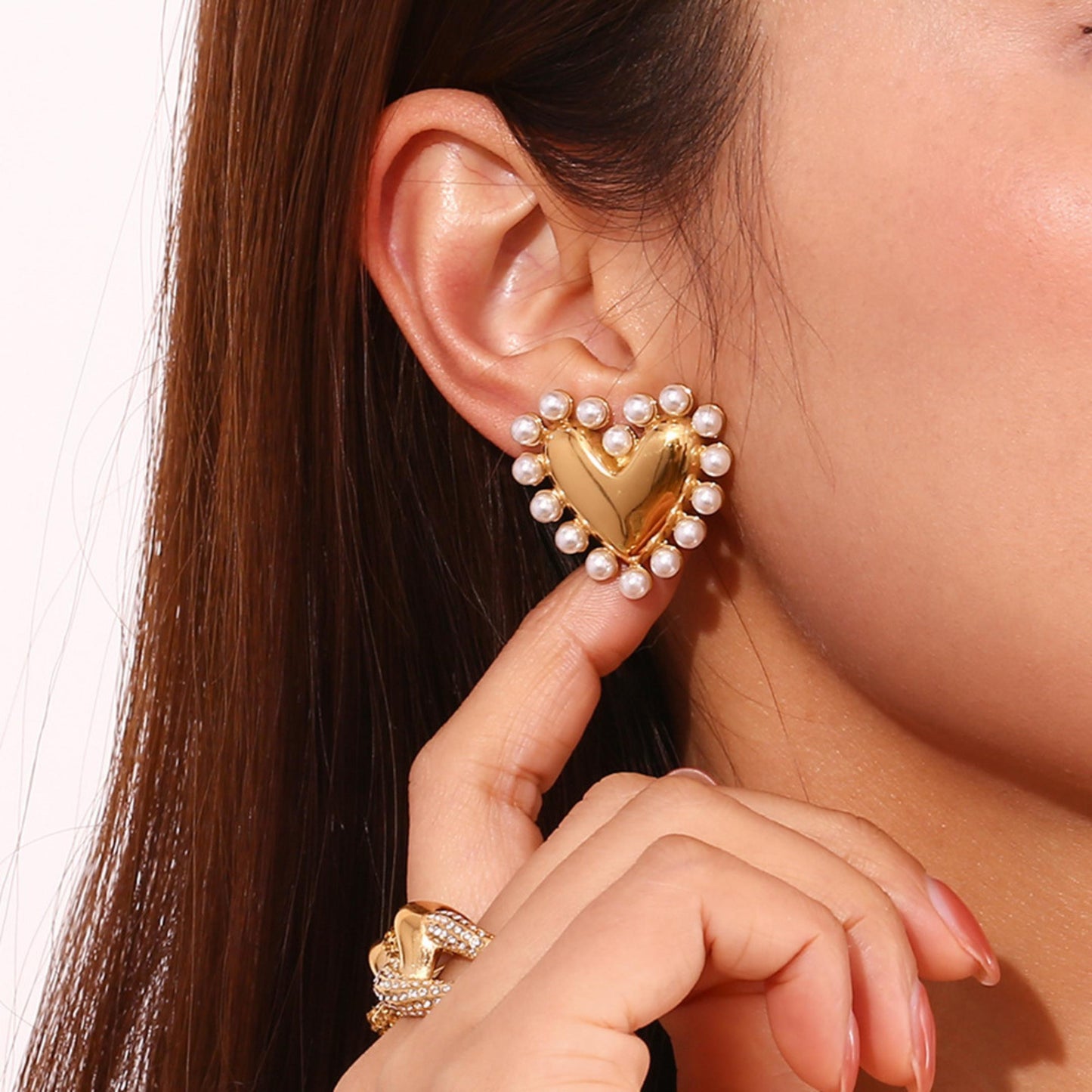 Heart-shaped gold earring with pearls worn by a person