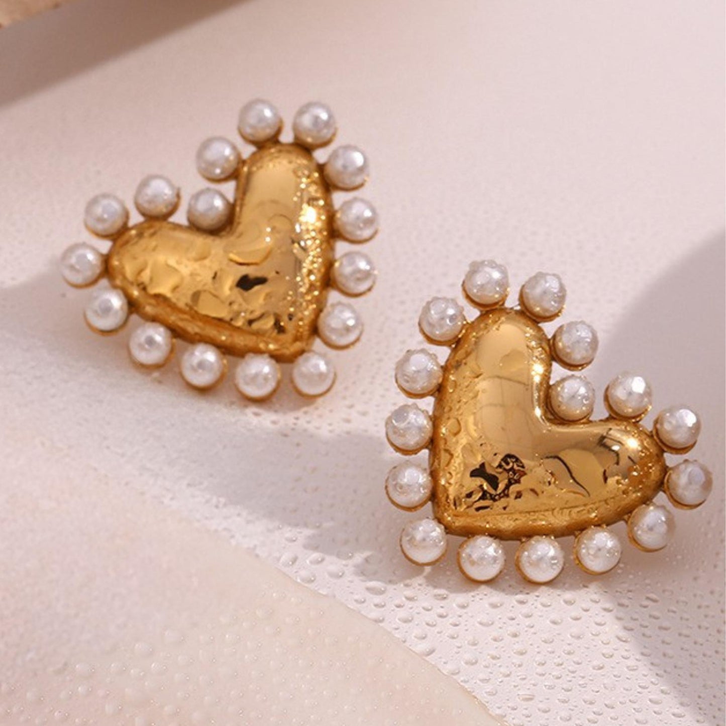 Gold heart-shaped earrings with pearl accents on a light pink background