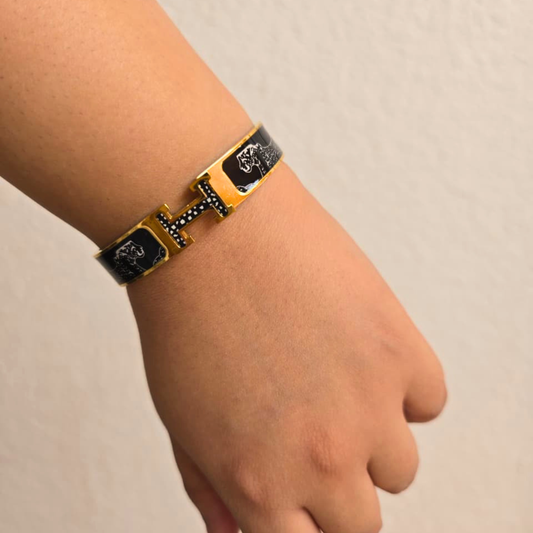Gold and black bracelet on a wrist against a beige background