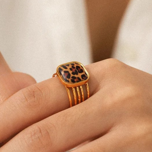 Gold ring with a leopard print design on a person's finger against a neutral background