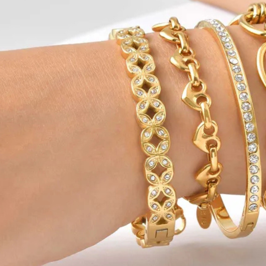 Gold bracelets with chain and heart designs on a wrist against a white background
