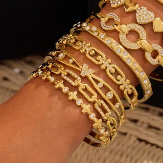 Gold bracelets with intricate designs on a wrist against a blurred background