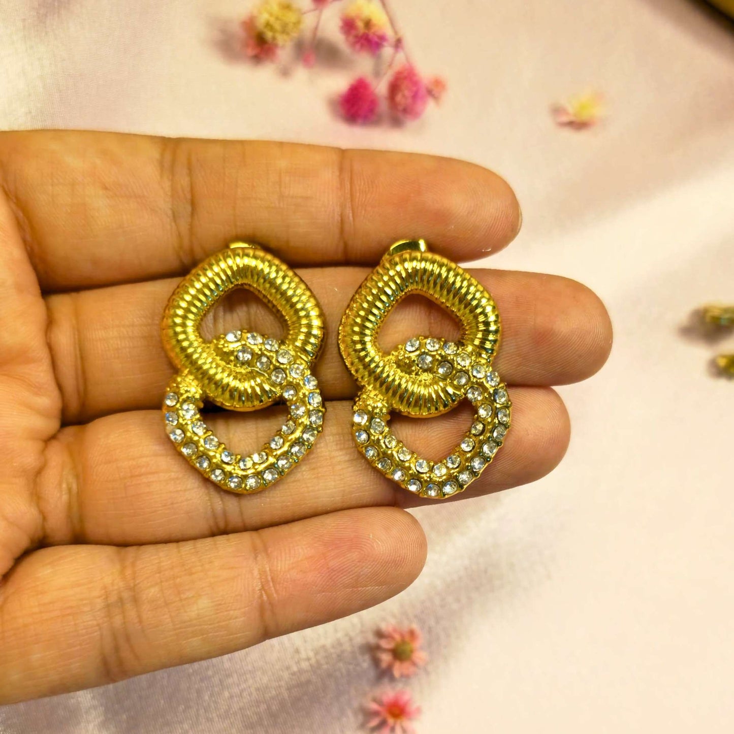 Gold earrings with interlocking square rings held in a hand against a light background