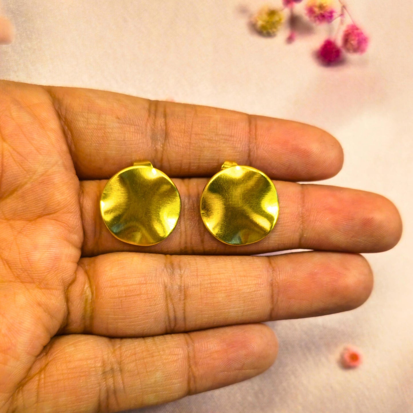 Gold round earrings held between fingers against a light background