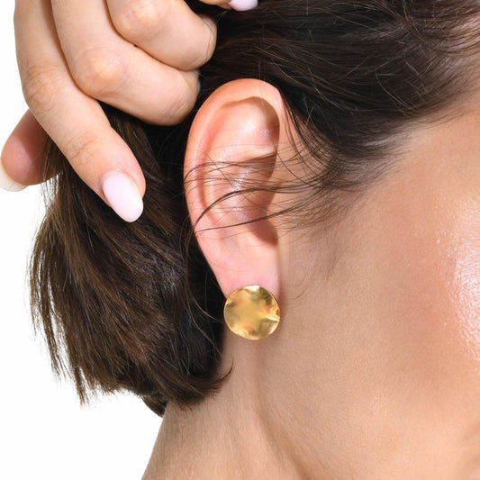Close-up of a person wearing a gold round earring with a hand adjusting hair.