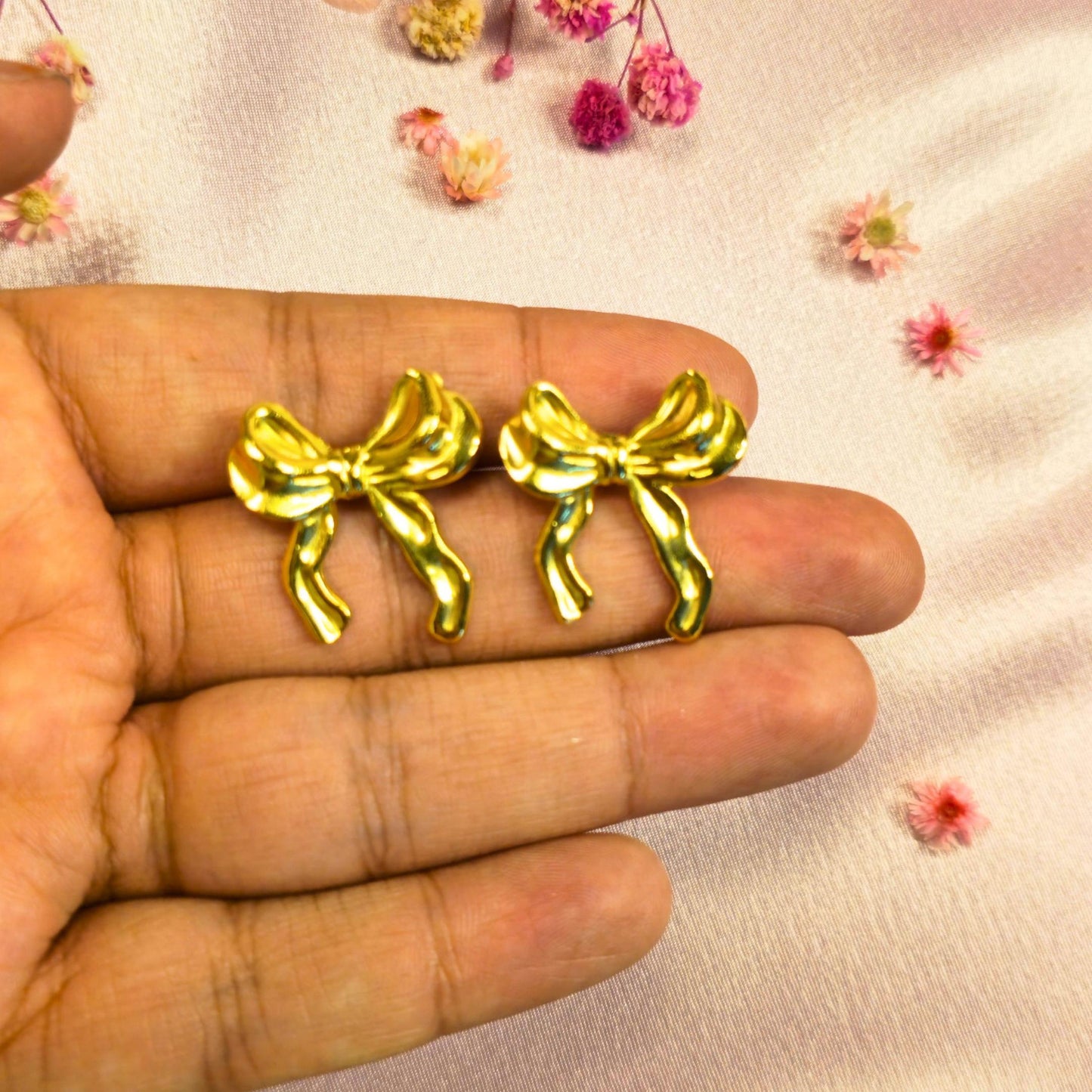 Gold bow-shaped earrings held between fingers with a light background