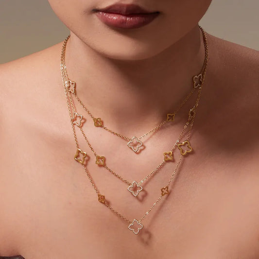 Close-up of a woman wearing a gold necklace with clover pendants on a neutral background