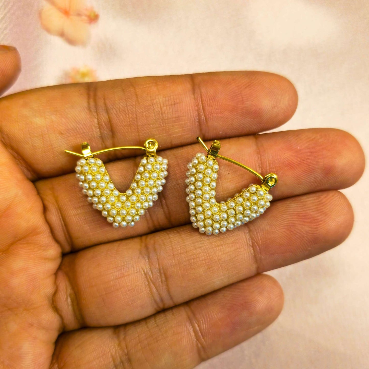 Gold and pearl heart-shaped earrings on a hand with a light background
