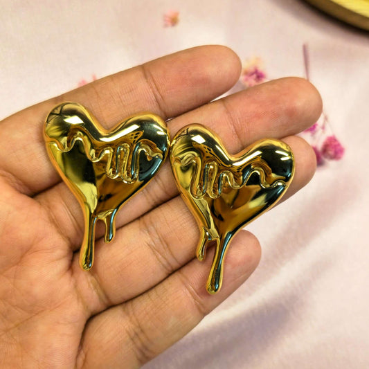 Gold drip heart-shaped earrings held in a hand with a blurred background