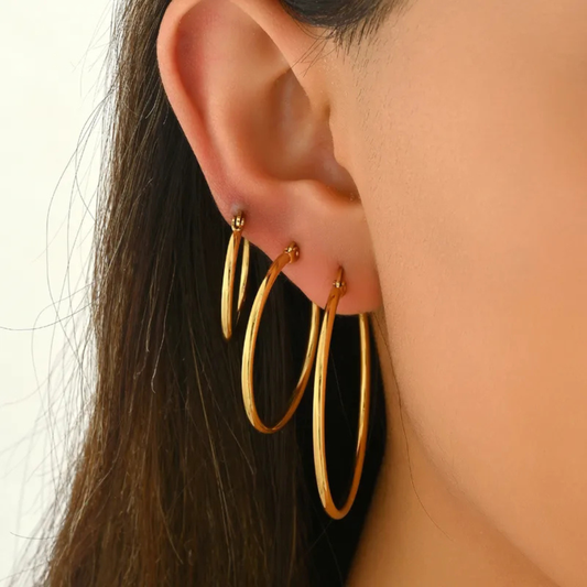 Gold hoop earrings worn by a person with dark hair.