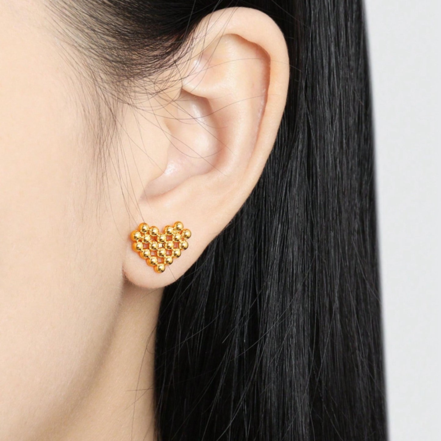 Gold heart-shaped beaded earring worn by a person with black hair.