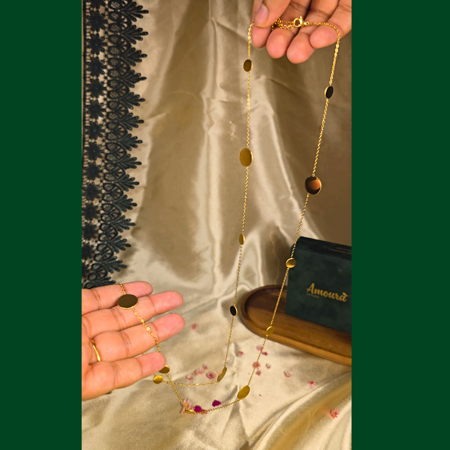 Gold necklace with gold beads held by a hand on a textured fabric background