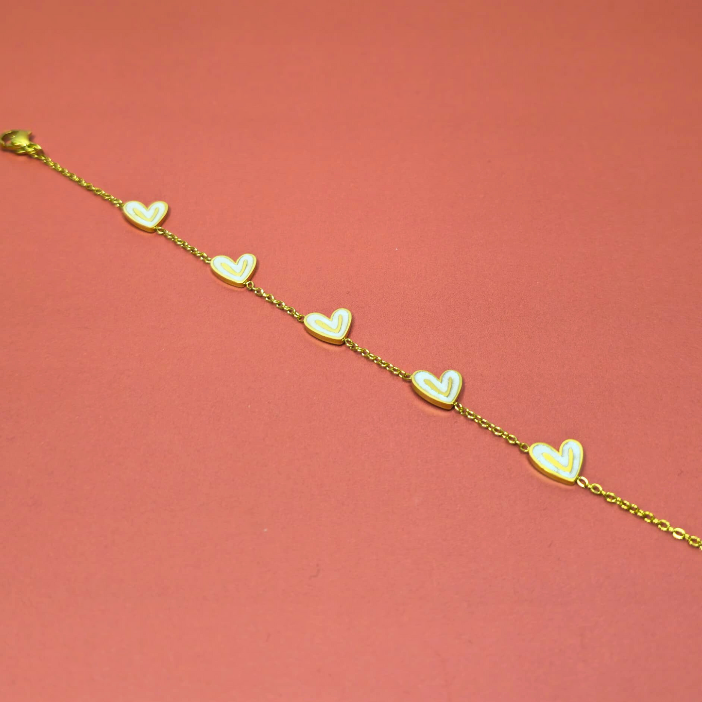 Gold bracelet with heart-shaped charms on a pink background