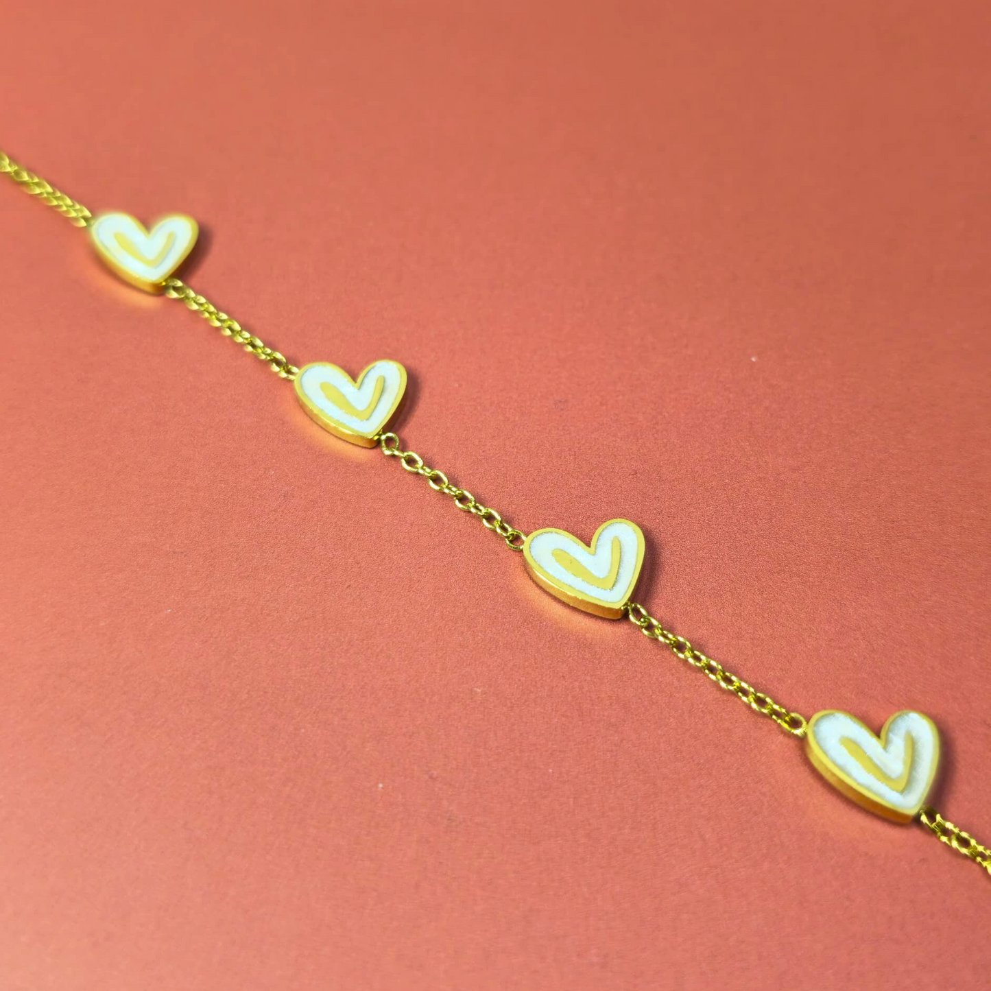 Gold bracelet with heart-shaped charms on a pink background