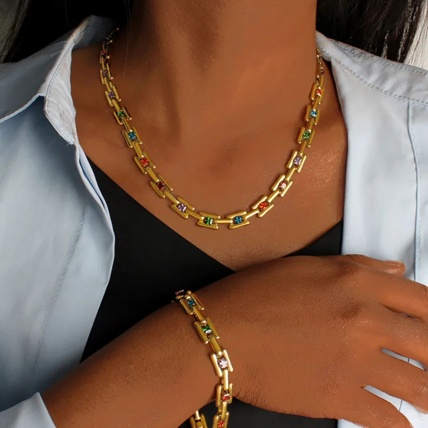 Gold chain necklace with colorful stones worn by a person.