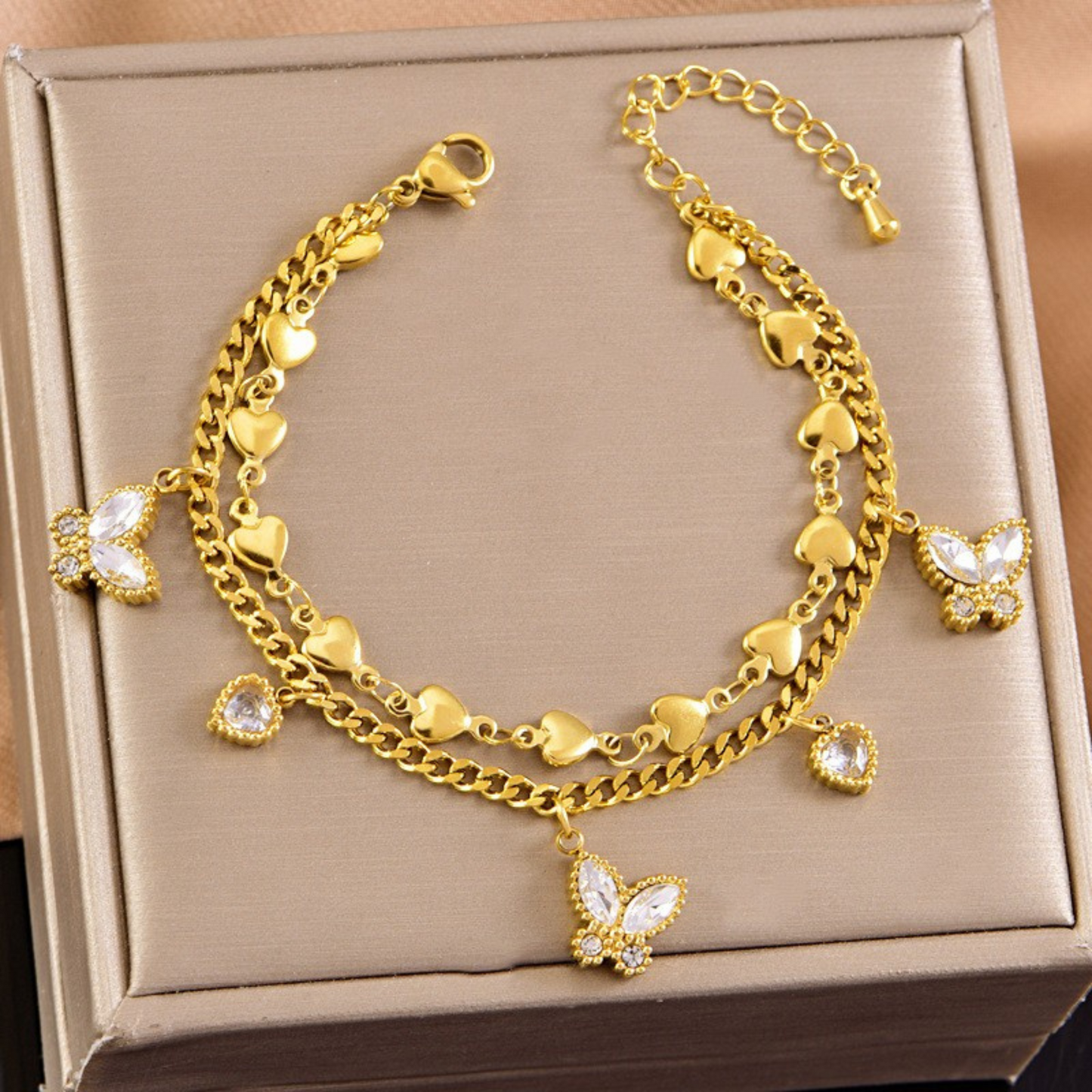 Gold bracelet with heart and butterfly charms on a beige box