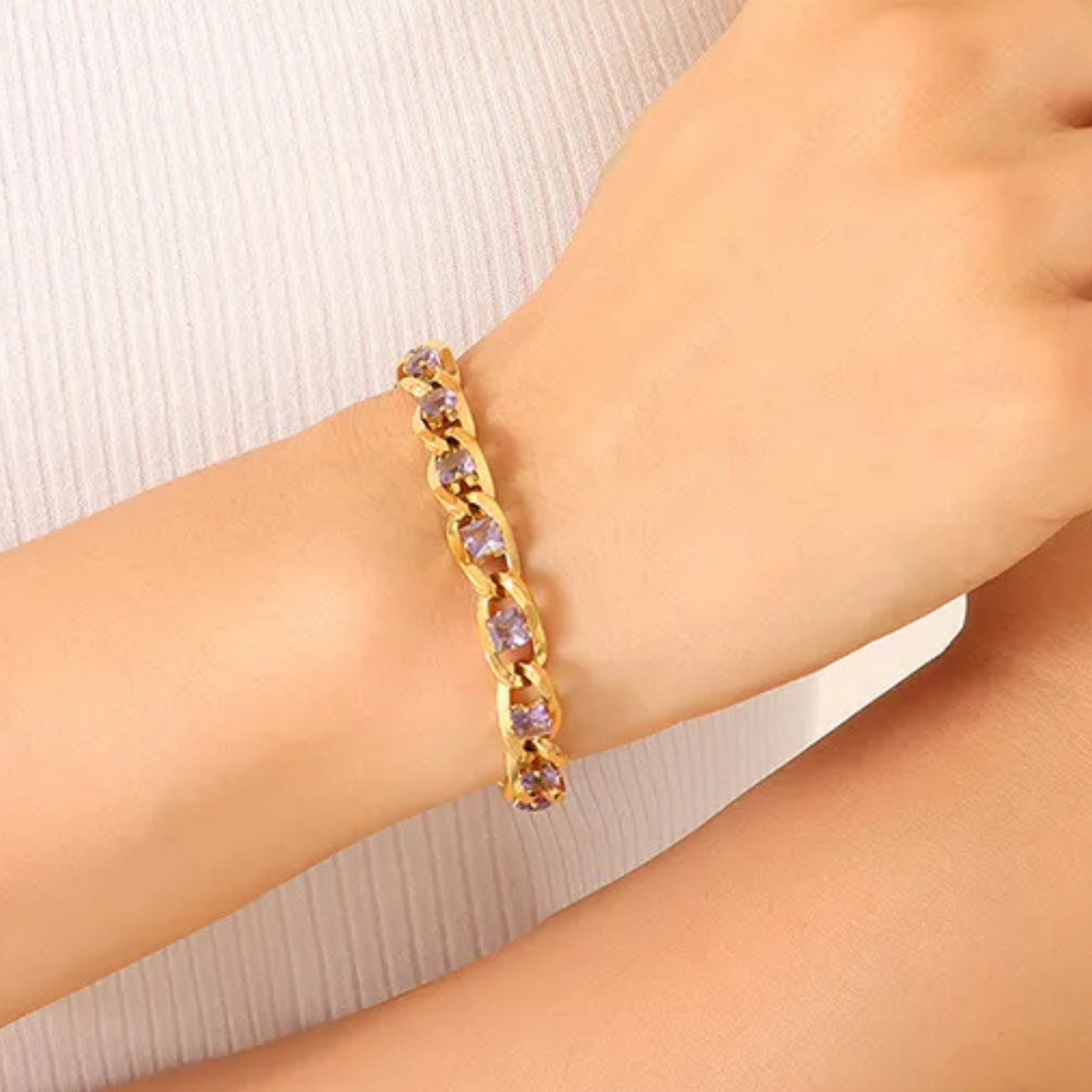 Gold bracelet with purple stones on a wrist against a white background
