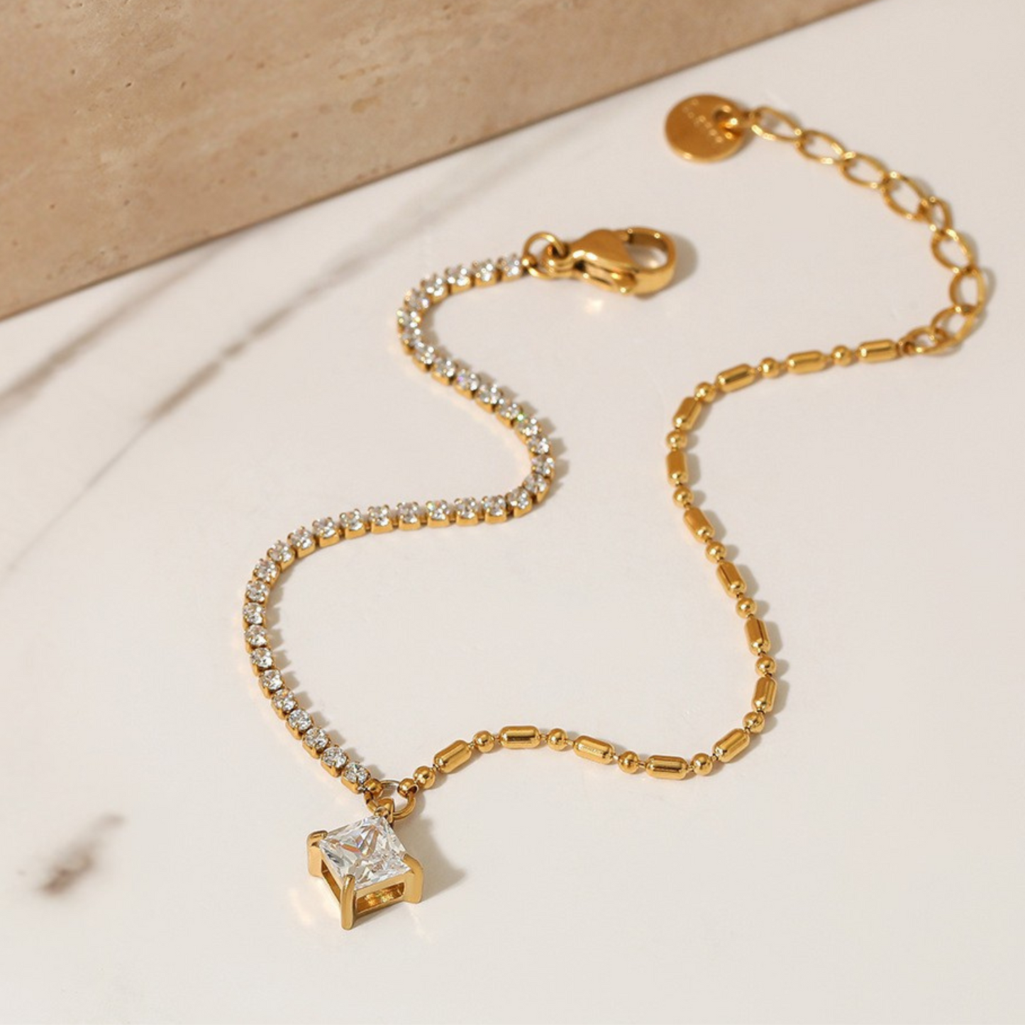 Gold bracelet with diamond charm on a beige background