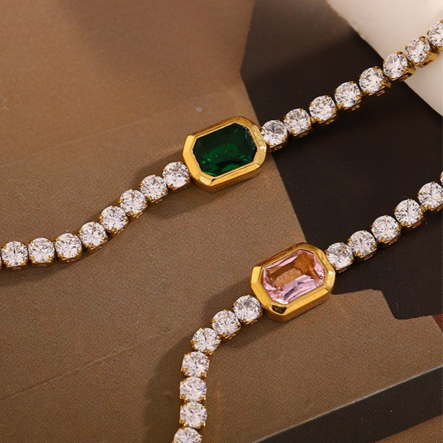 Two gold bracelets with gemstones on a brown surface
