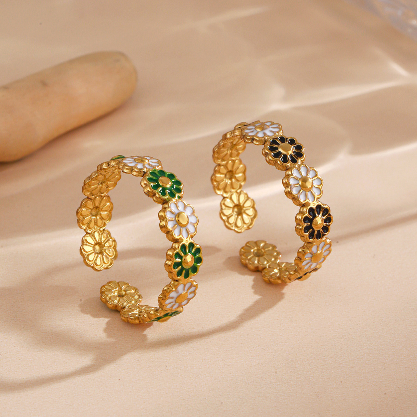 Gold floral bangles with green and black accents on a beige background