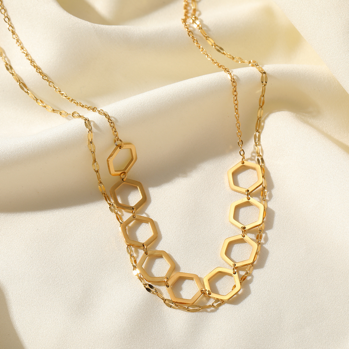 Gold hexagonal chain necklace on a beige fabric background