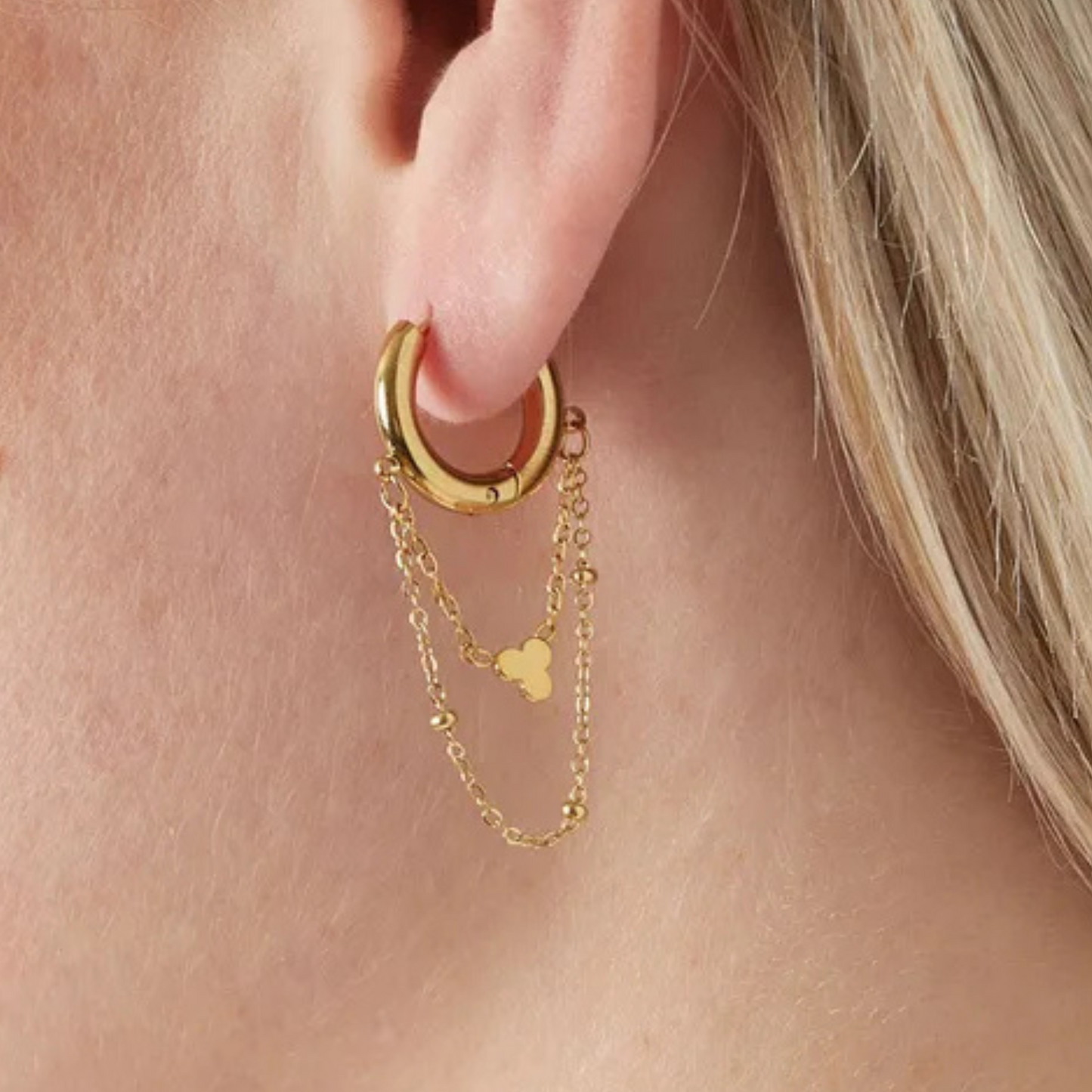 Gold hoop earring with chain detail worn by a person