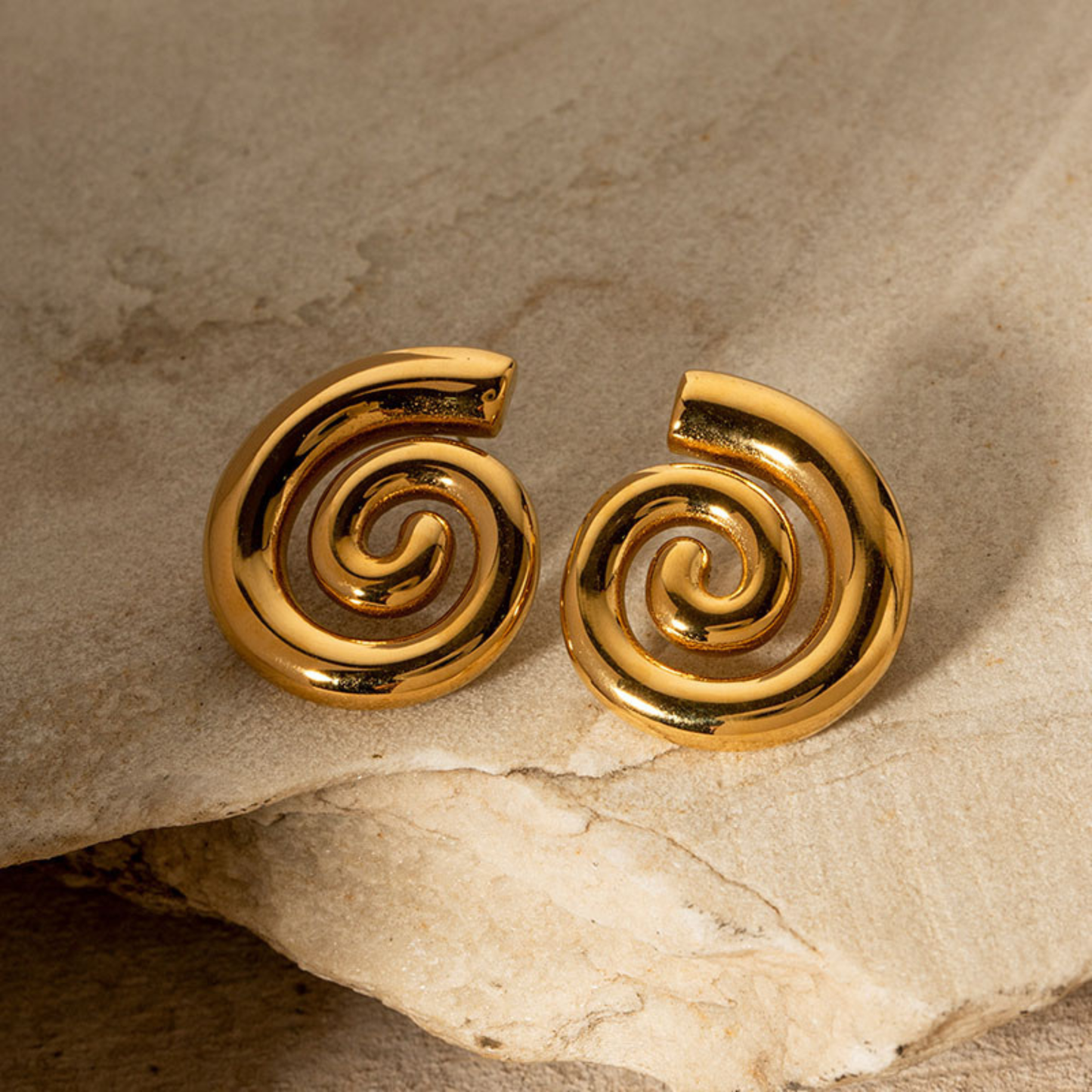 Pair of gold spiral earrings on a stone surface