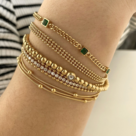 Multiple gold bracelets with green gemstones on a wrist against a neutral background