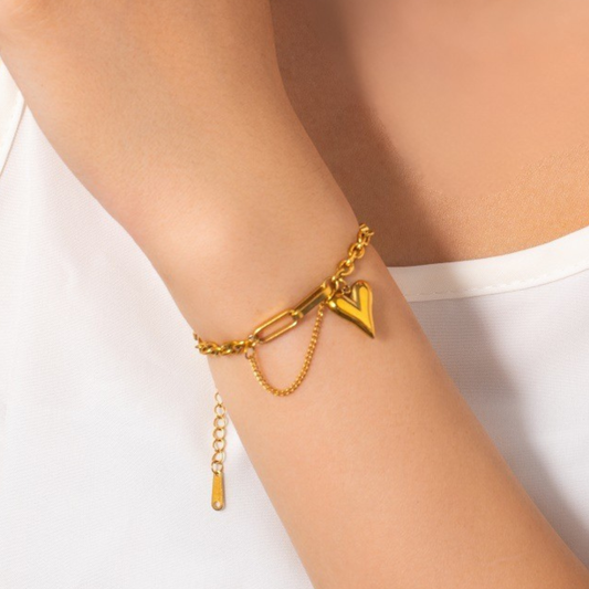 Gold bracelet with a heart charm on a person's wrist against a white background