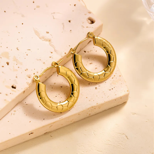 Gold hoop earrings on a textured beige surface