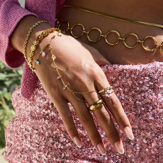 Close-up of a hand wearing gold jewelry with a pink sequin dress background