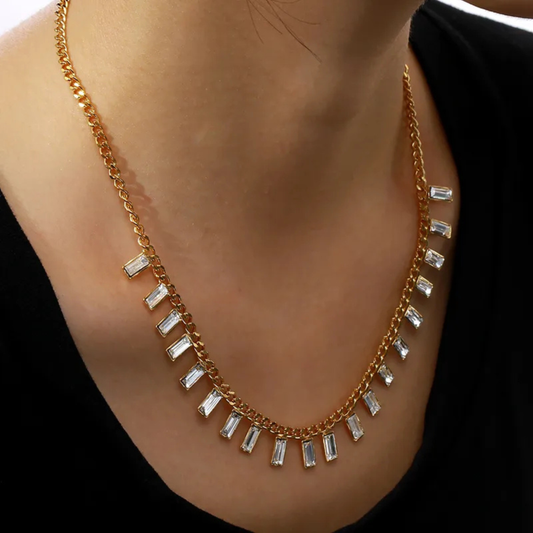 Gold necklace with rectangular gemstones worn by a person against a black background