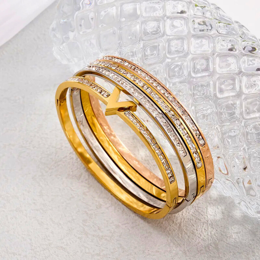 Three gold bangles with diamond accents on a textured white surface