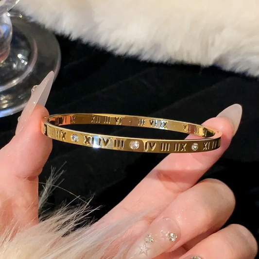 Gold bracelet with Roman numeral design held by a hand against a fur background