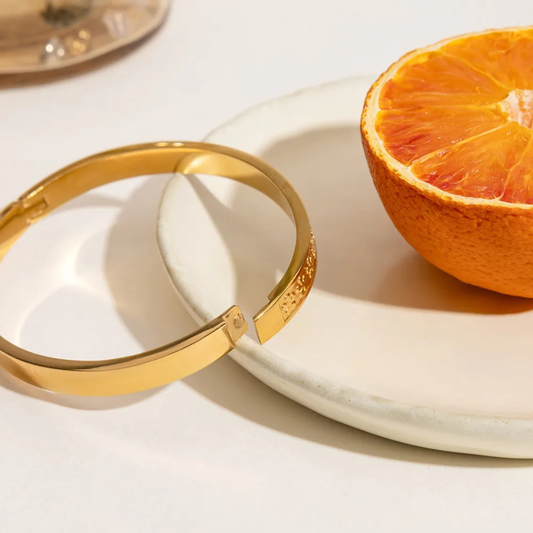 Gold bracelet on a white plate with an orange half