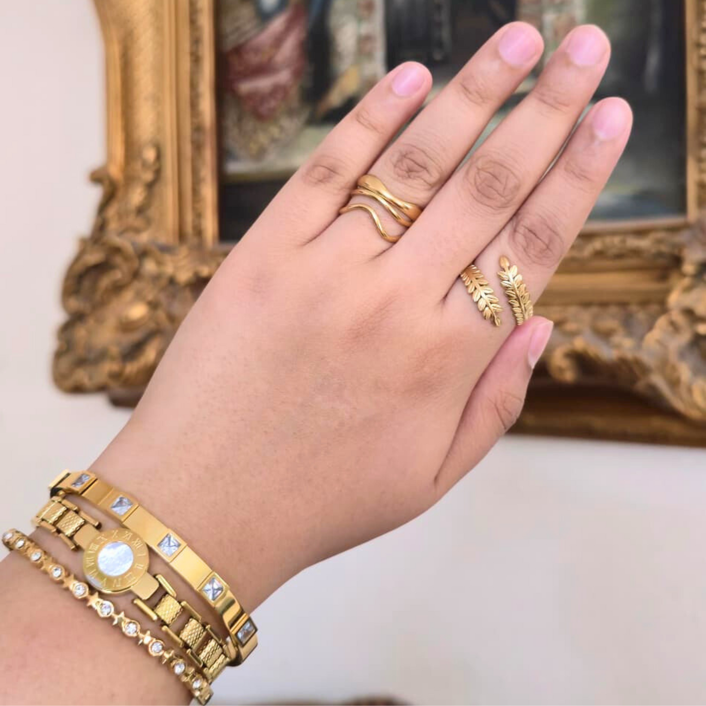 Hand wearing gold jewelry with a decorative background