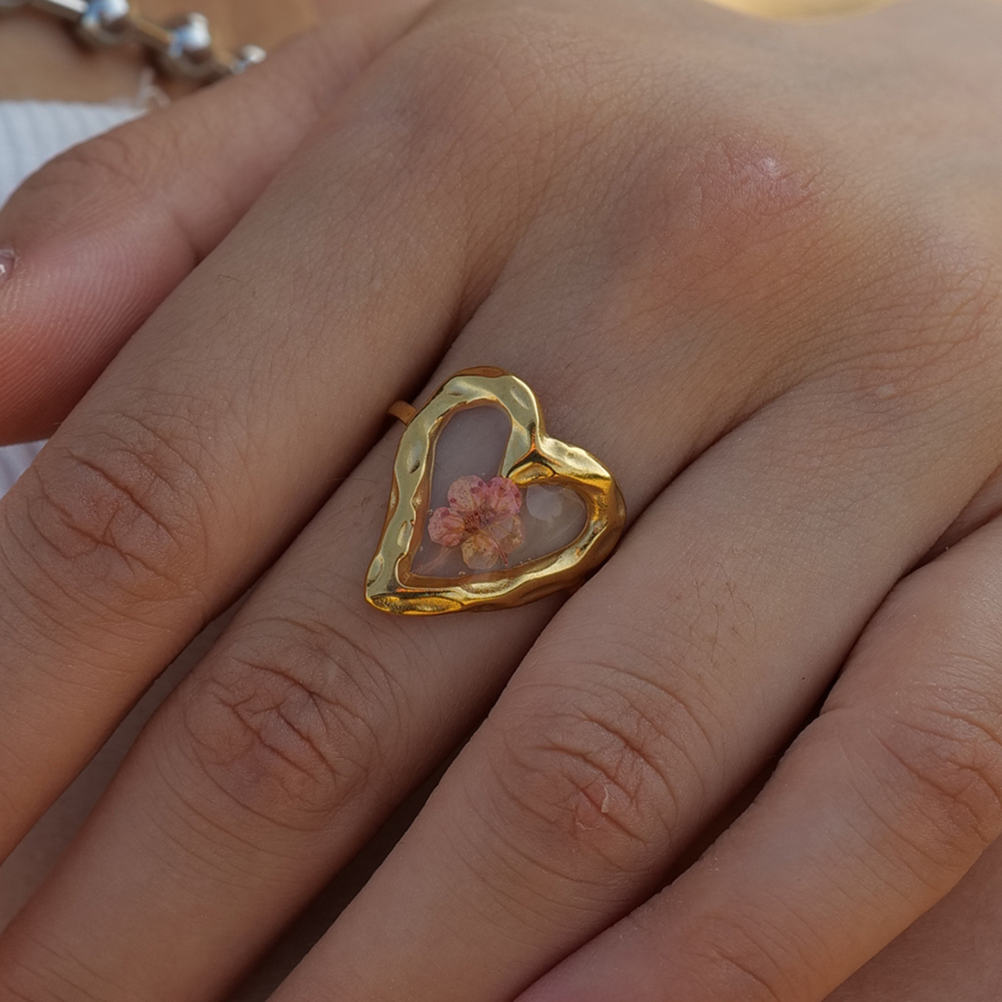 Gold heart-shaped ring with a floral design on a person's finger