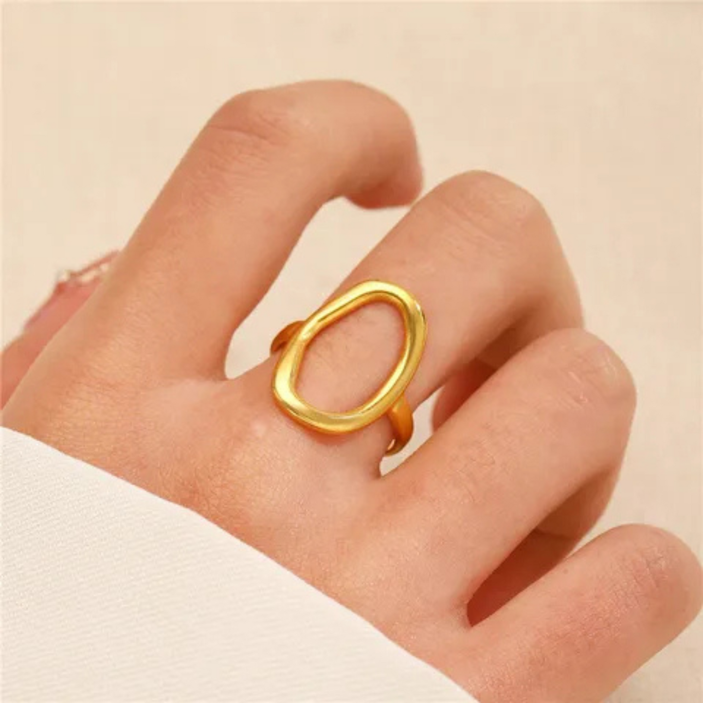 Gold ring on a hand against a beige background