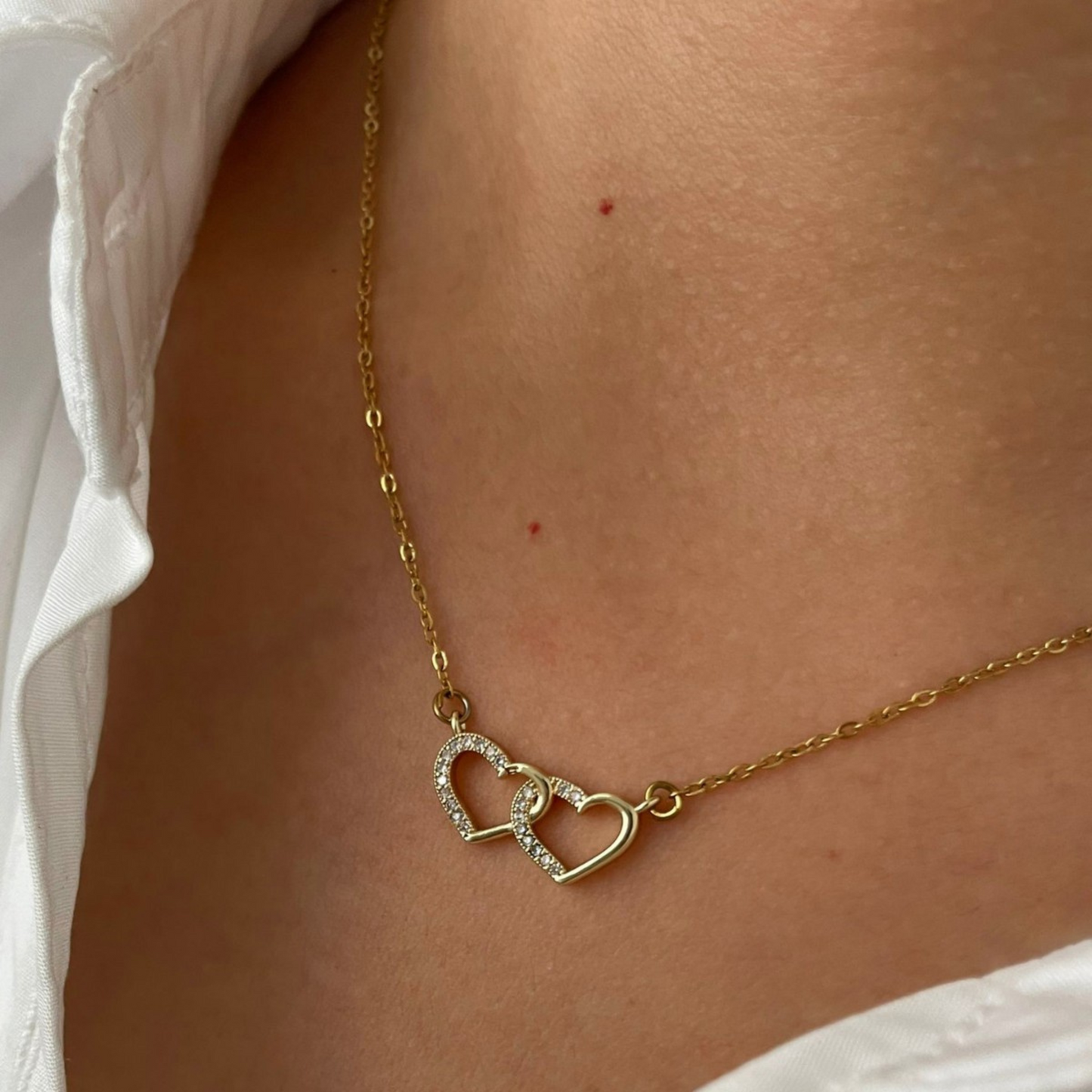 Gold necklace with heart pendants on a person wearing a white shirt.