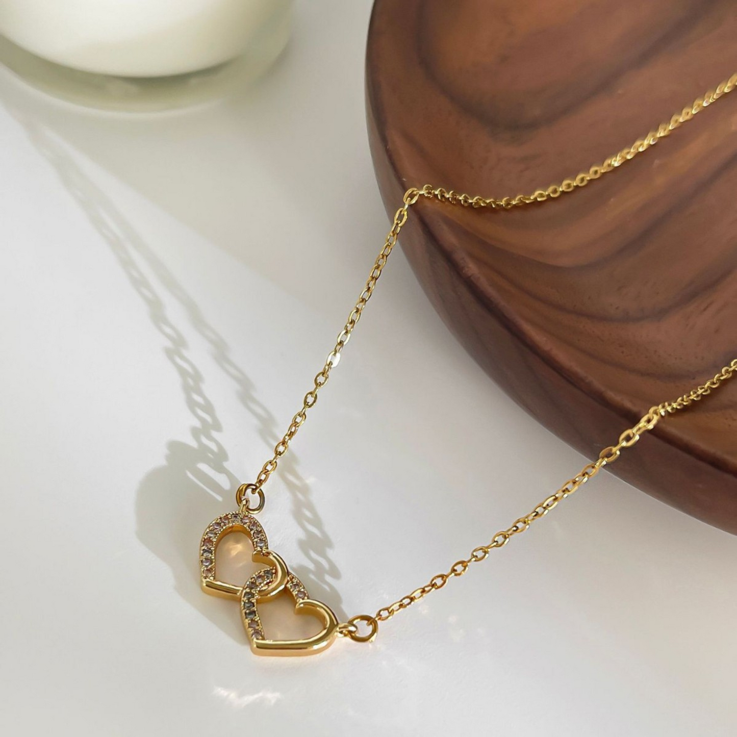 Gold necklace with heart-shaped links on a white surface with a wooden block in the background