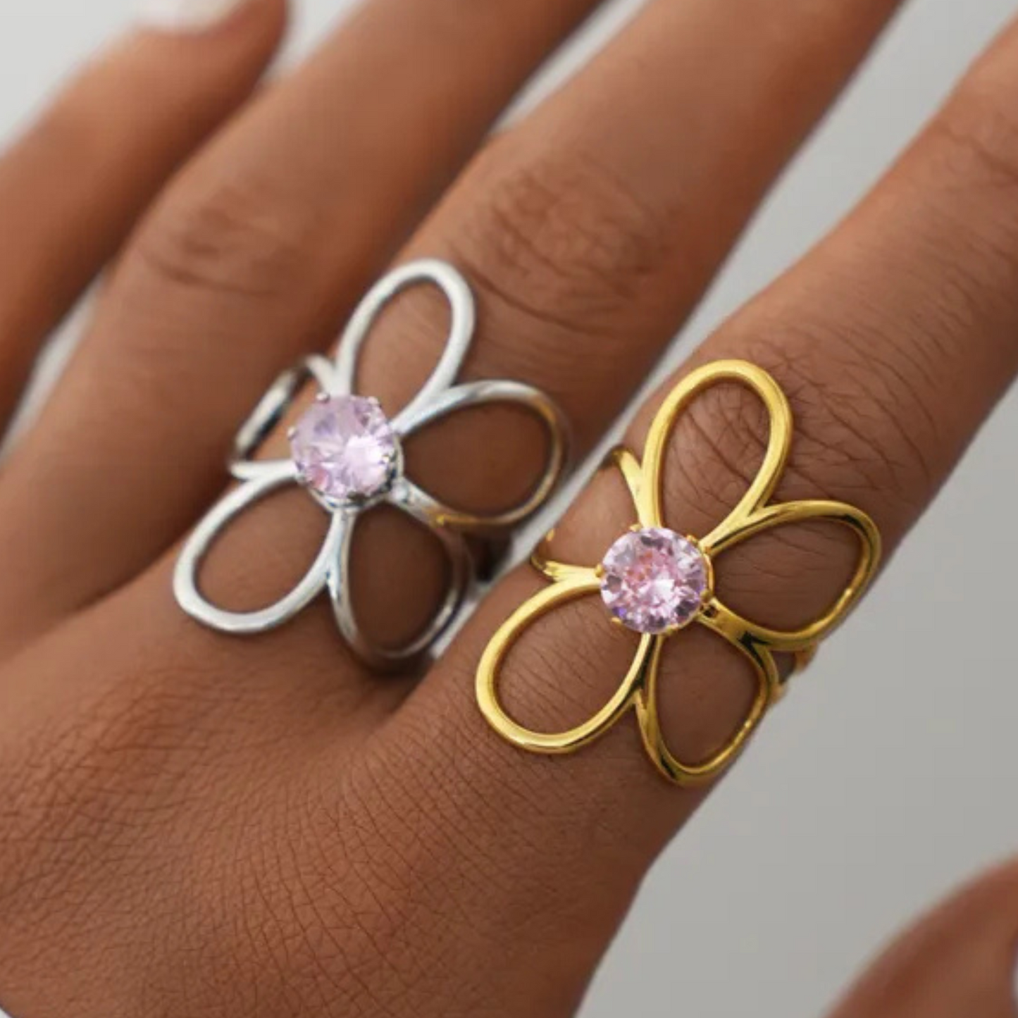 Two flower-shaped rings, one gold and one silver, with pink gemstones on a hand.