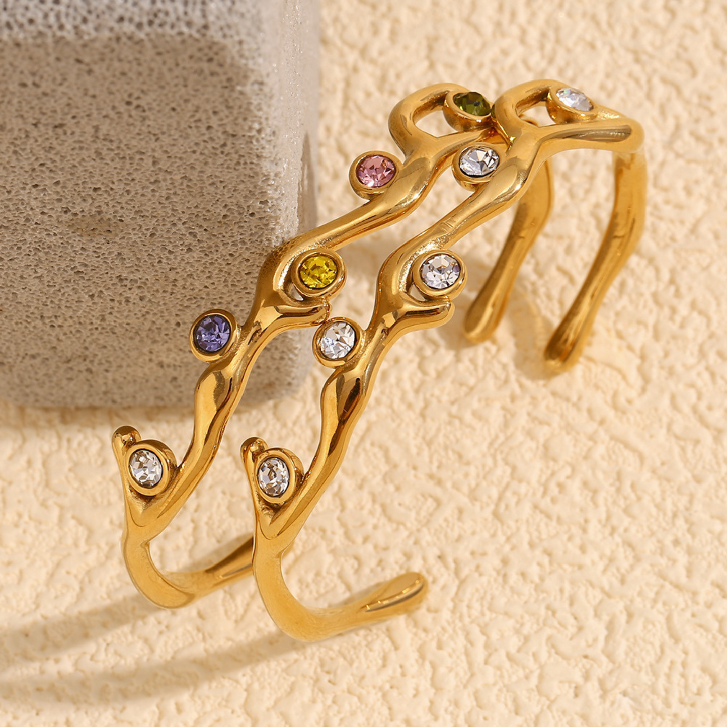 Gold bracelet with embedded colorful gemstones on a textured beige background
