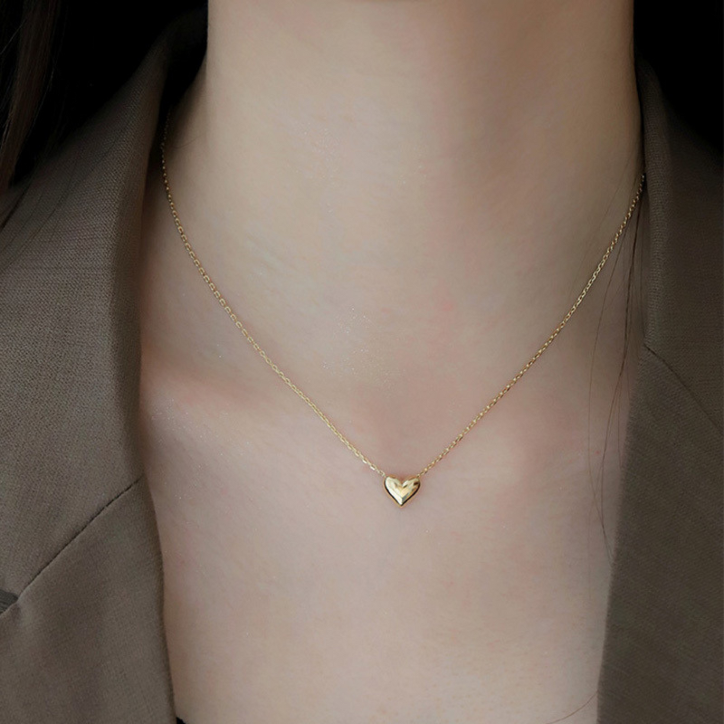 Gold heart necklace on a person's neck against a neutral background