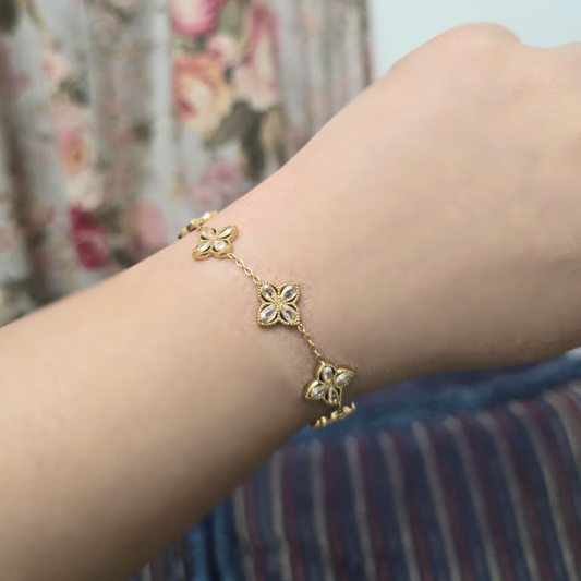 Gold bracelet with floral designs on a wrist against a floral curtain background