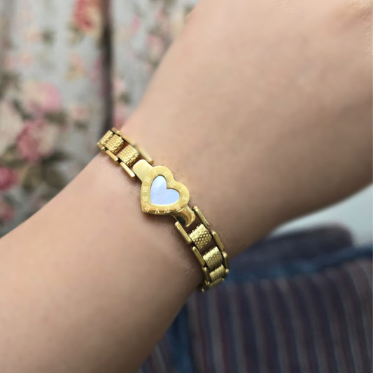 Gold bracelet with a heart-shaped charm on a wrist against a floral background