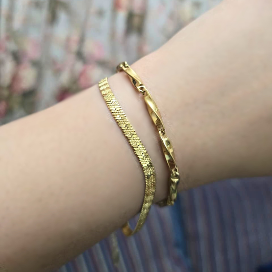 Gold bracelets on a wrist with a blurred floral background